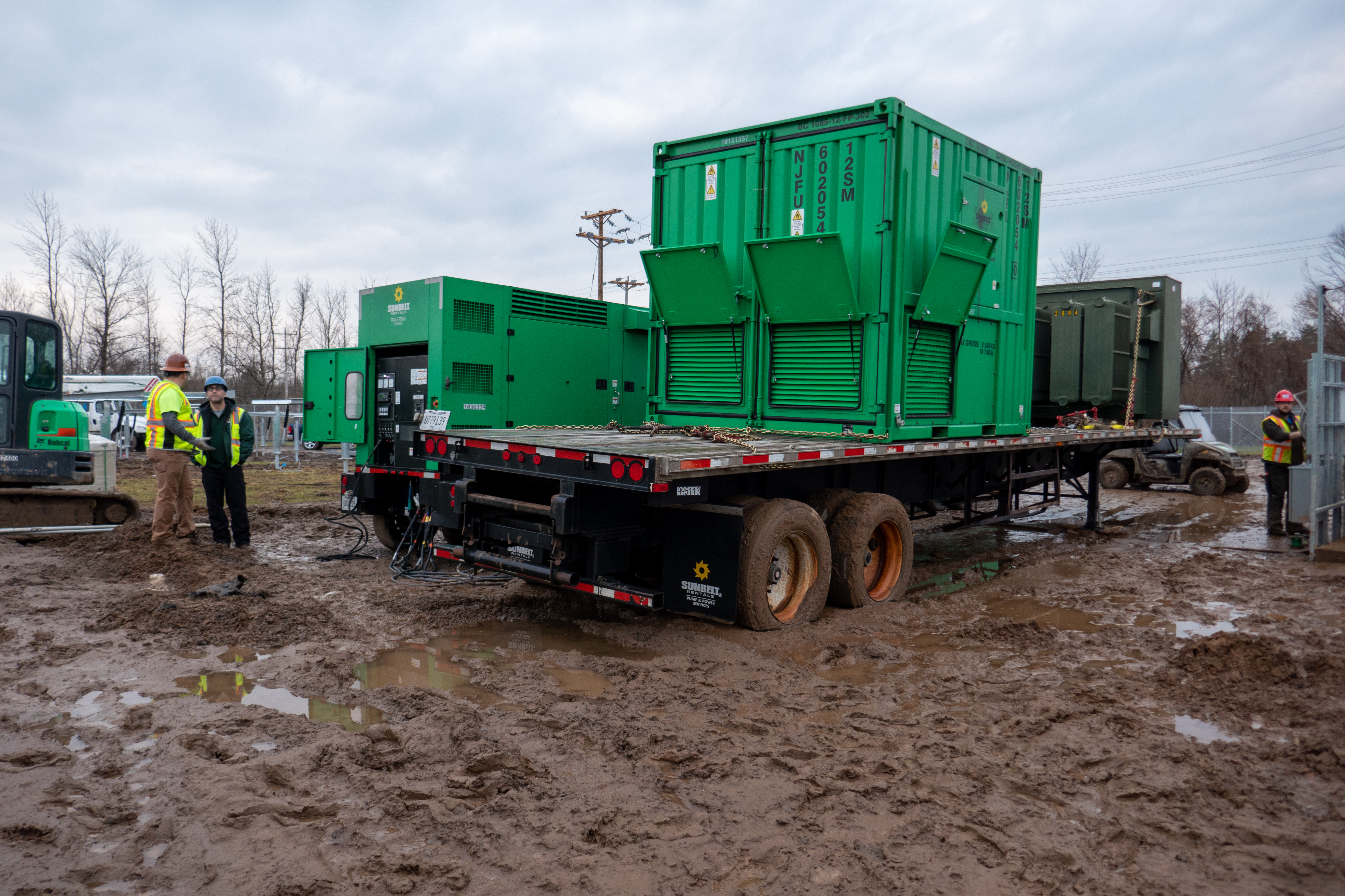A flatbed trailer parked at a muddy construction site, carrying Sunbelt Rentals load banks.