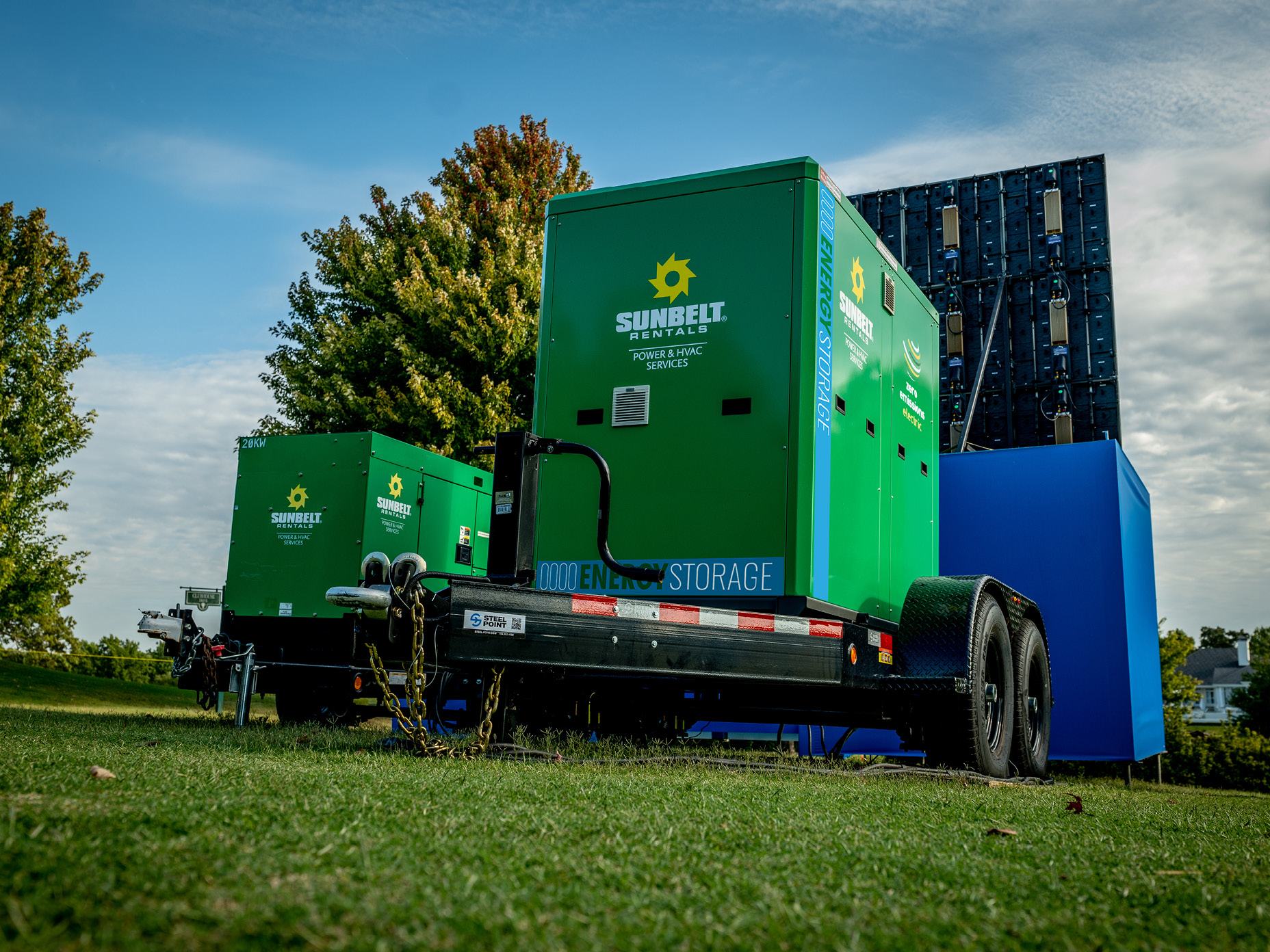 Two green Sunbelt Rentals generator units are positioned on trailers in a grassy outdoor area.