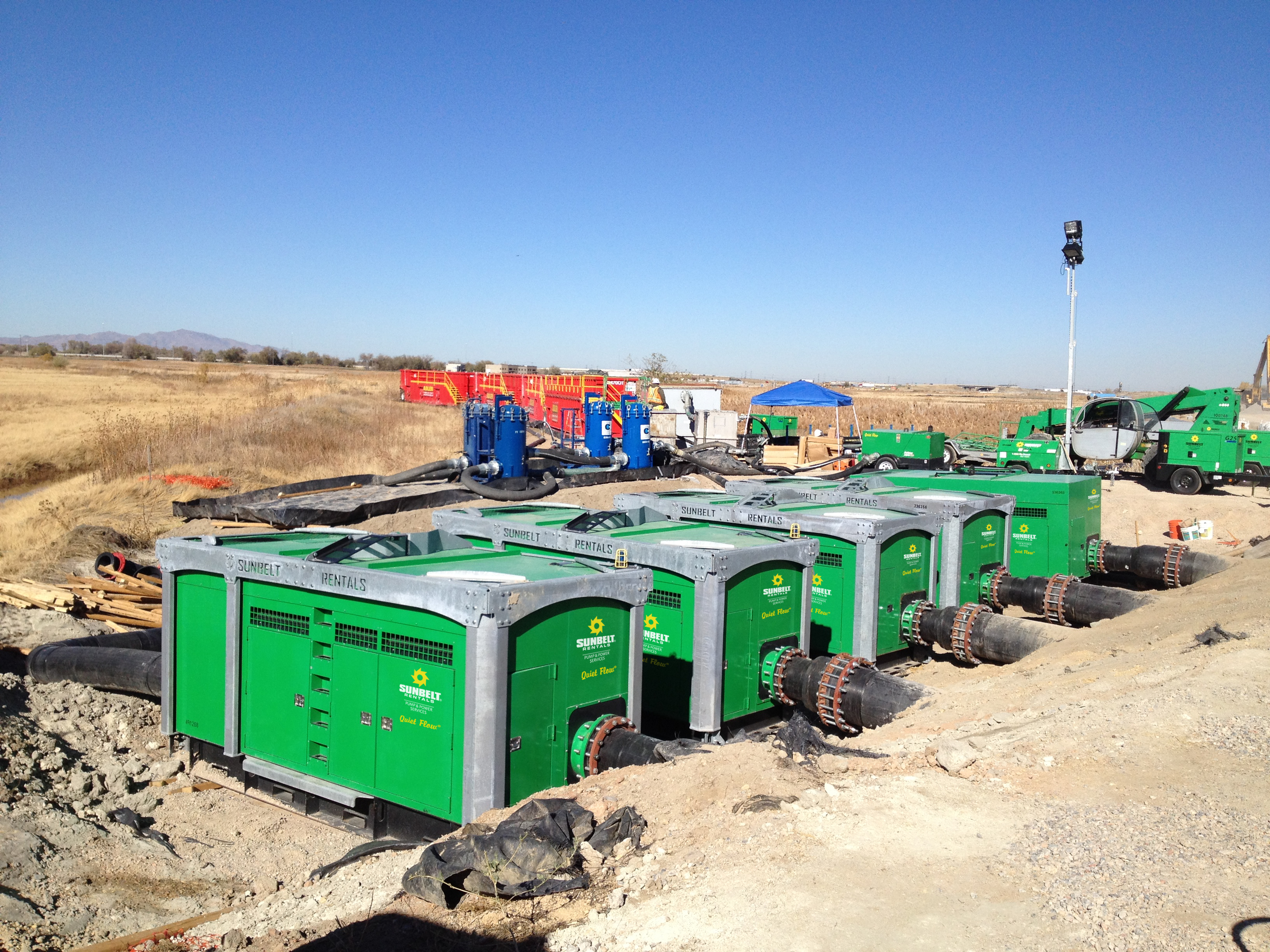 A row of industrial bypass pumps from Sunbelt Rentals at an outdoor construction site.
