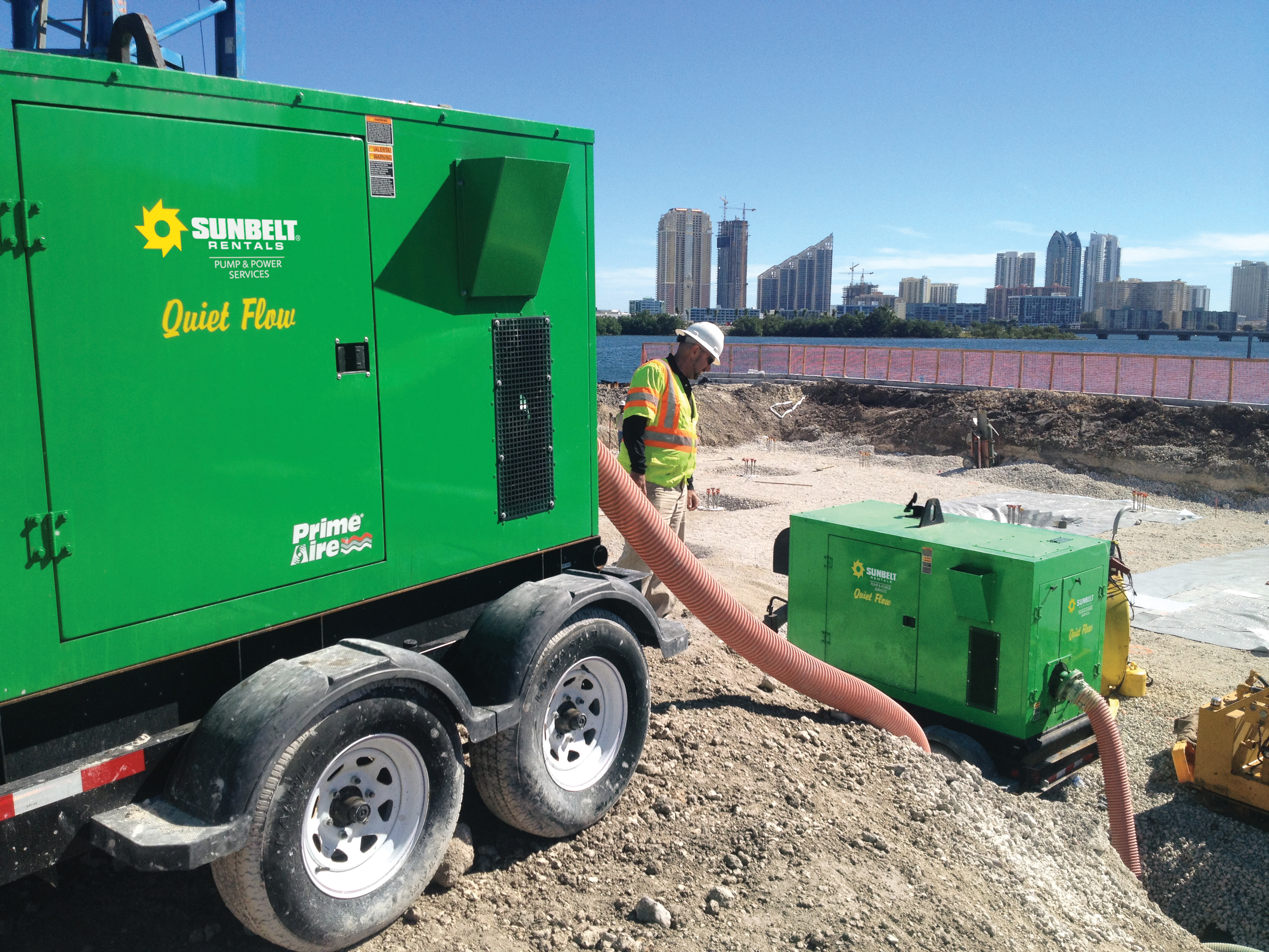 A construction worker in safety gear beside Sunbelt Rentals Quiet Flow pumps at a construction site.