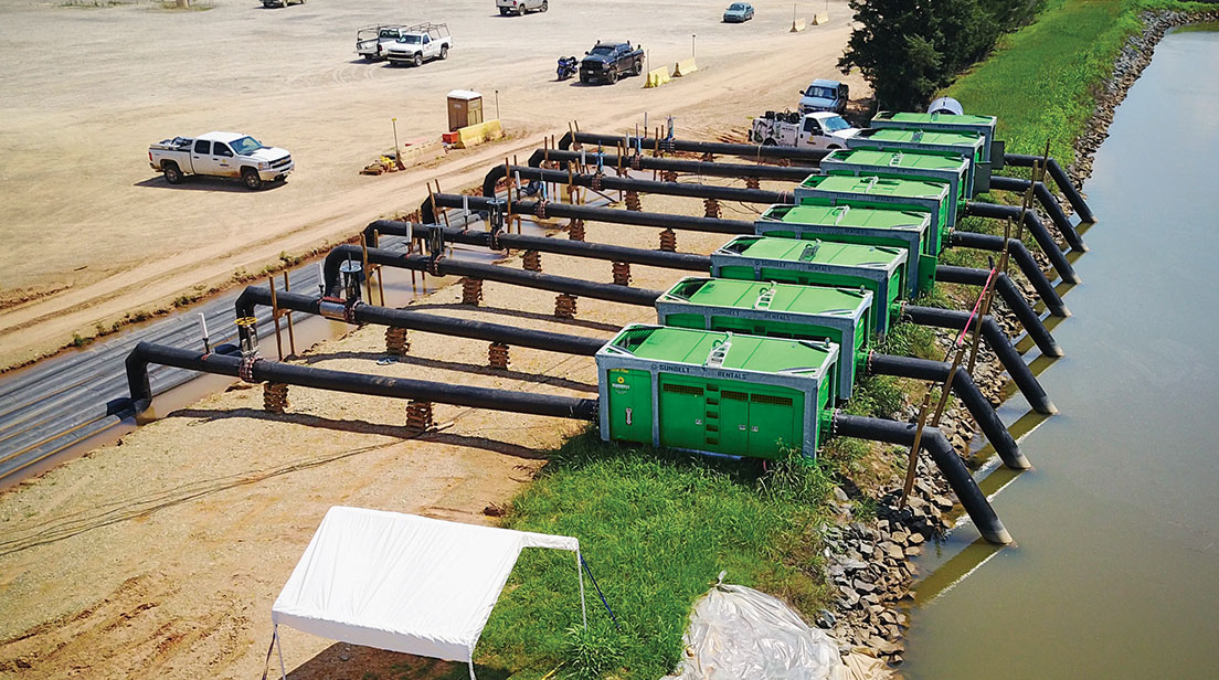 A row of pumps from Sunbelt Rentals positioned along a body of water. 