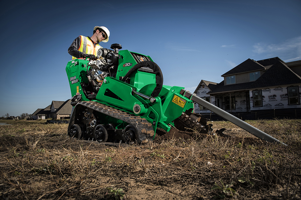 Someone operating a trencher at a residential job site.