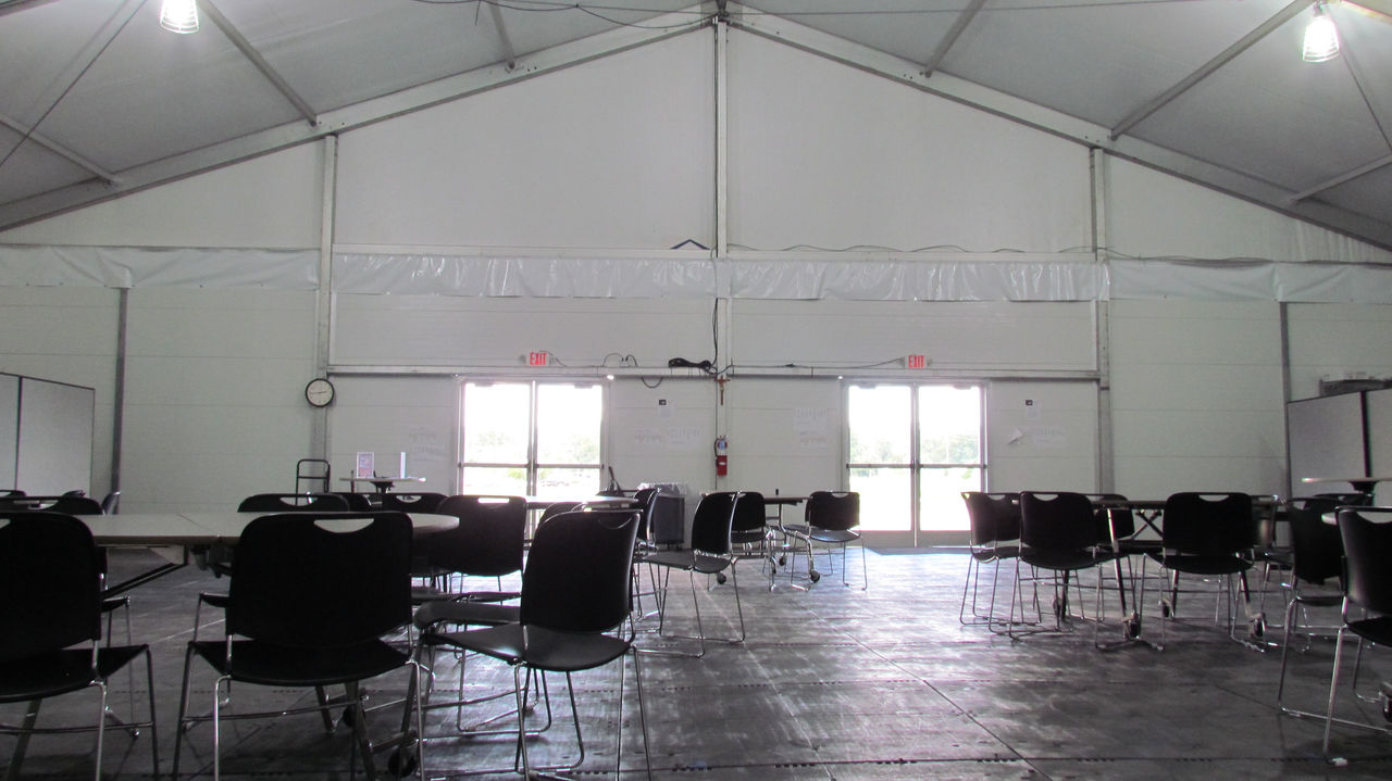 Tables and chairs set up inside of a tension fabric structure.