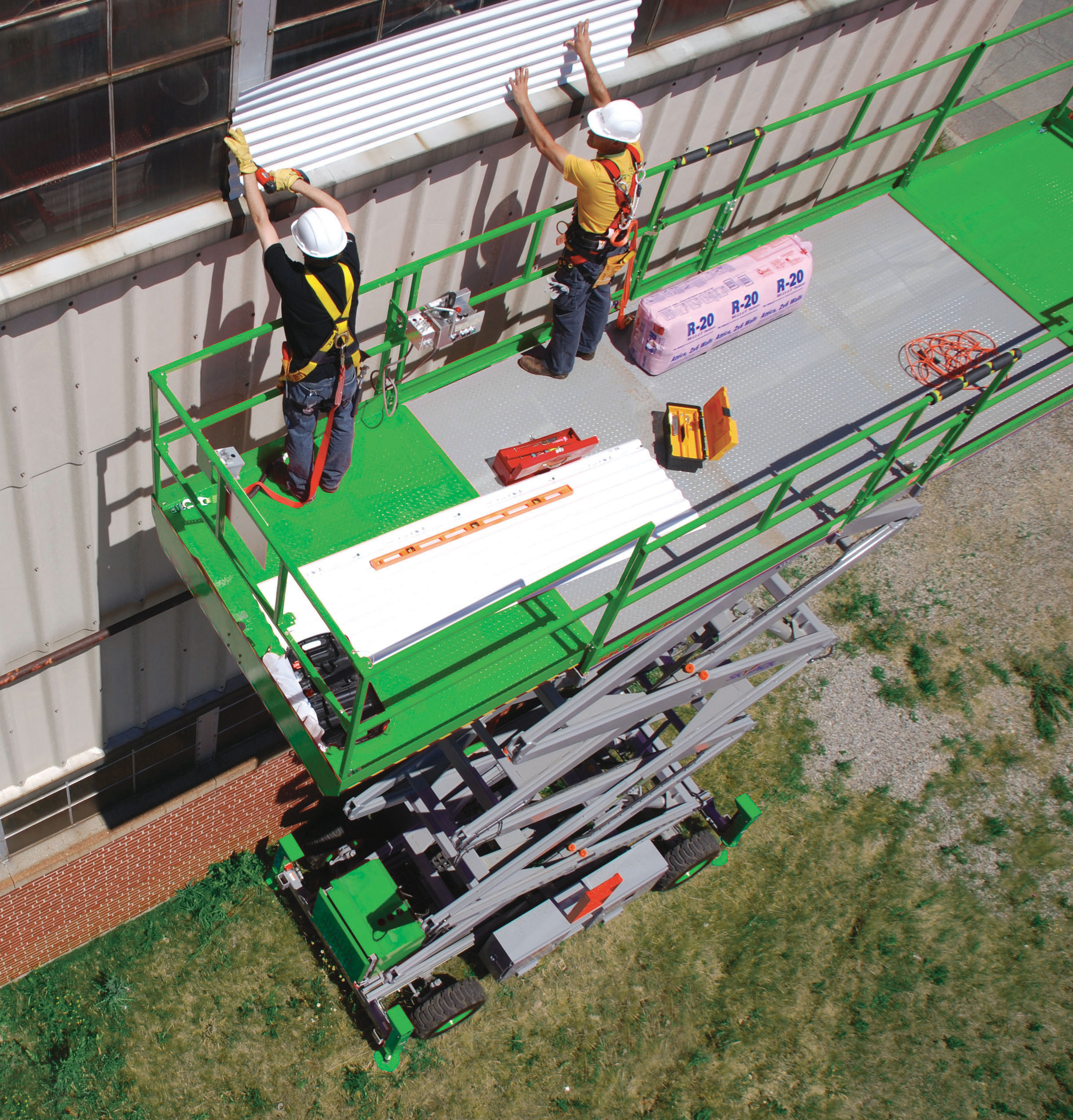 Two people on a large scissor lift, working on the side of a building.