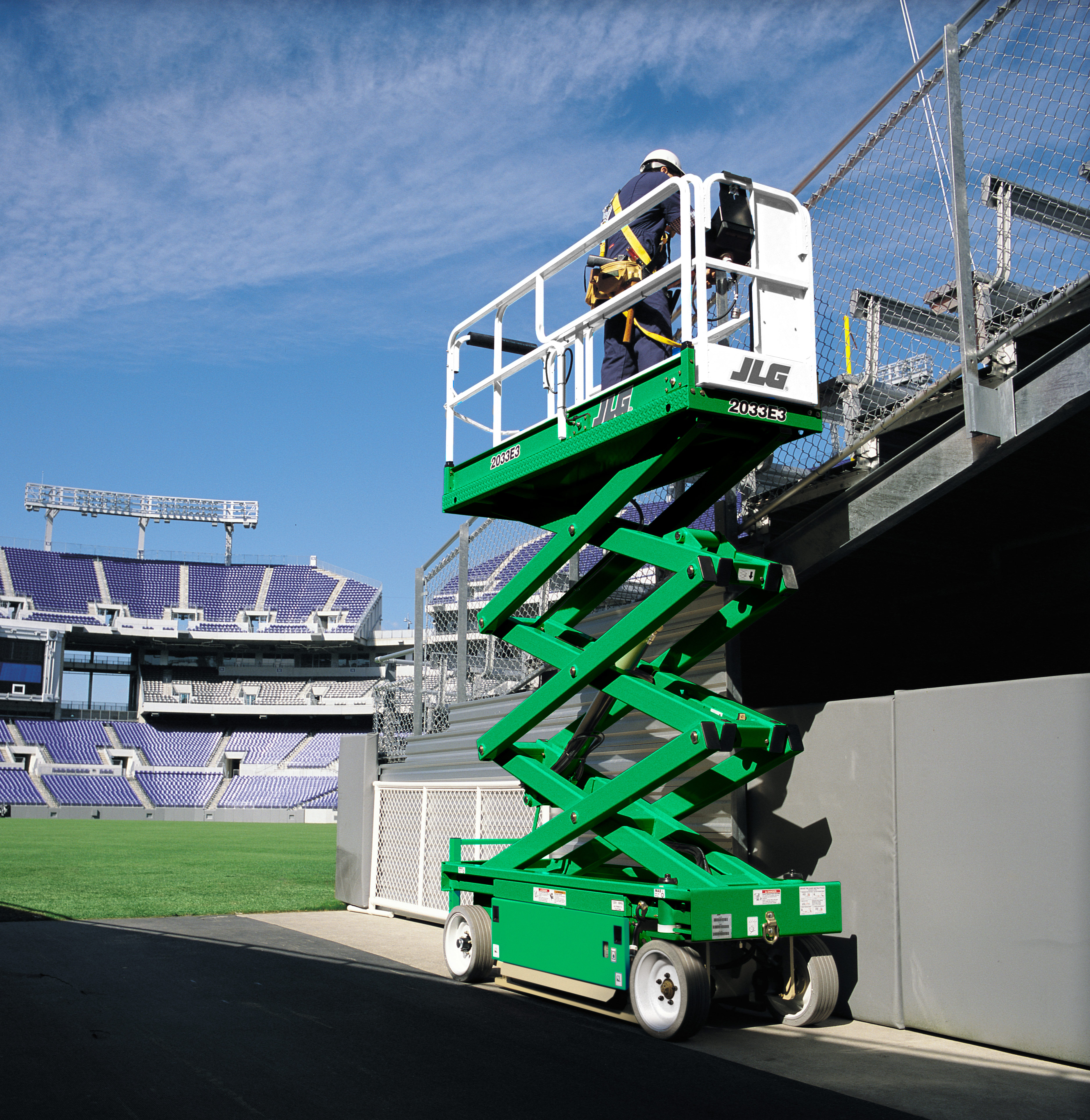 Someone operating a scissor lift alongside stands at a stadium.