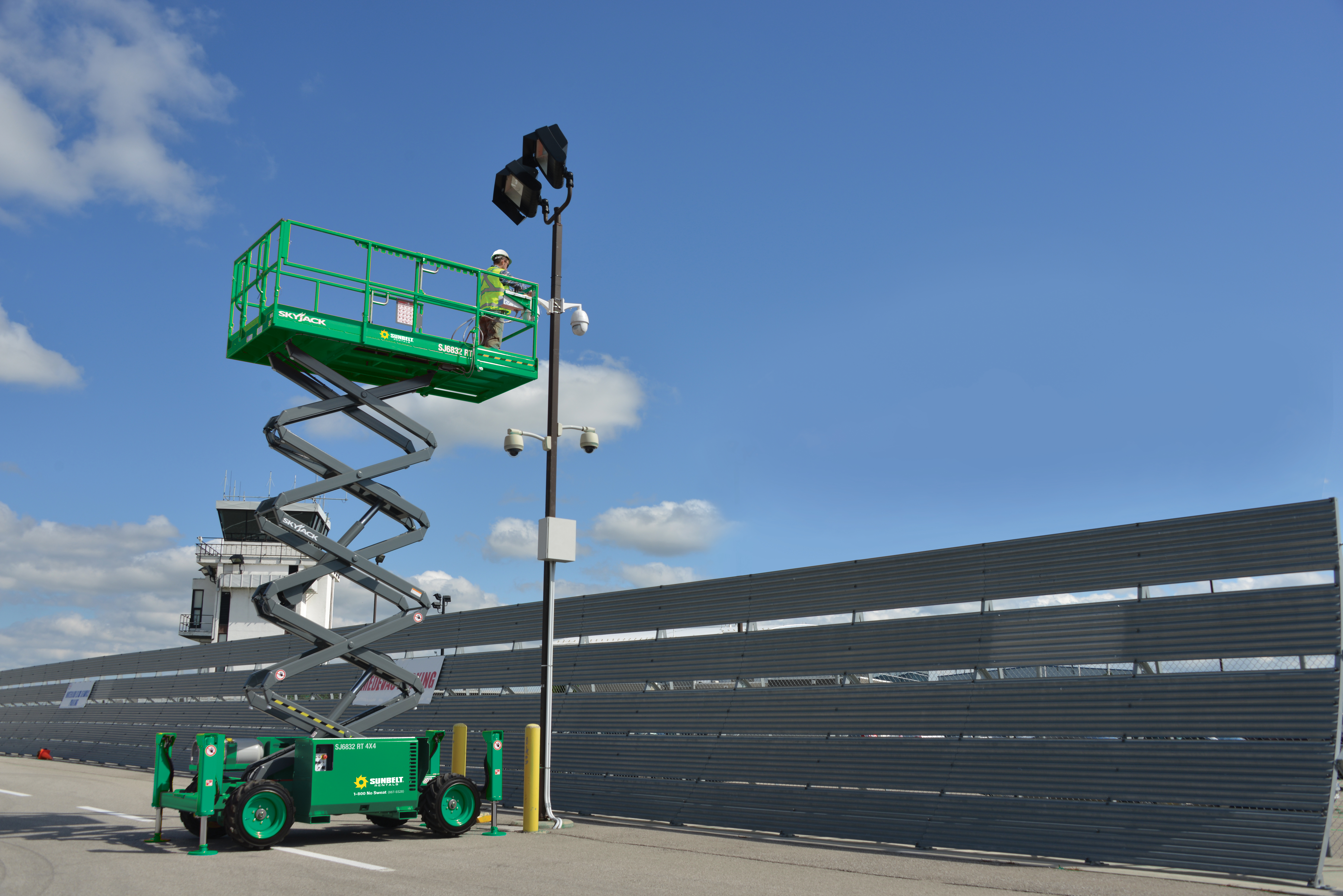 Someone operating a scissor lift next to a light pole.