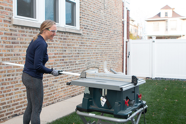 Person wearing safety glasses and gloves using a table saw in a backyard.